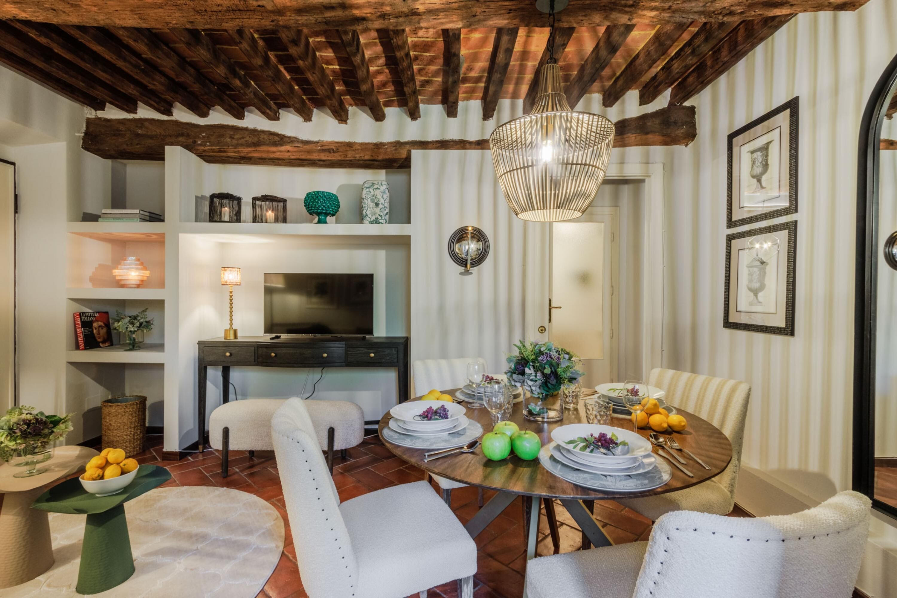 Un coin repas avec un plafond en bois, une table ronde dressée pour quatre personnes et un téléviseur en arrière-plan.