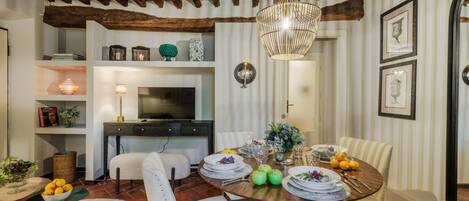 Un coin repas avec un plafond en bois, une table ronde dressée pour quatre personnes et un téléviseur en arrière-plan.