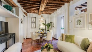 Una sala de estar moderna con techo de madera, paredes blancas, un comedor con mesa redonda y un sofá con cojines verdes.