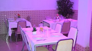 Un espace repas avec des tables dressées pour quatre personnes, chacune étant recouverte d’une nappe blanche et agrémentée de chaises et de la vaisselle de base.