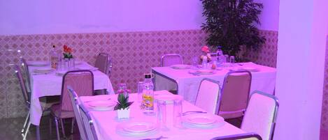 A dining area with tables set for four, each with white tablecloths, chairs, and basic tableware.