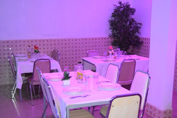 A dining area with tables set for four, each with white tablecloths, chairs, and basic tableware. - Hotel berges du Sine (Fatick)