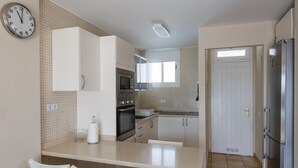 A kitchen with a dining table, chairs, a clock, and a refrigerator. - Alsol Las Perlas (San Bartolomé de Tirajana)
