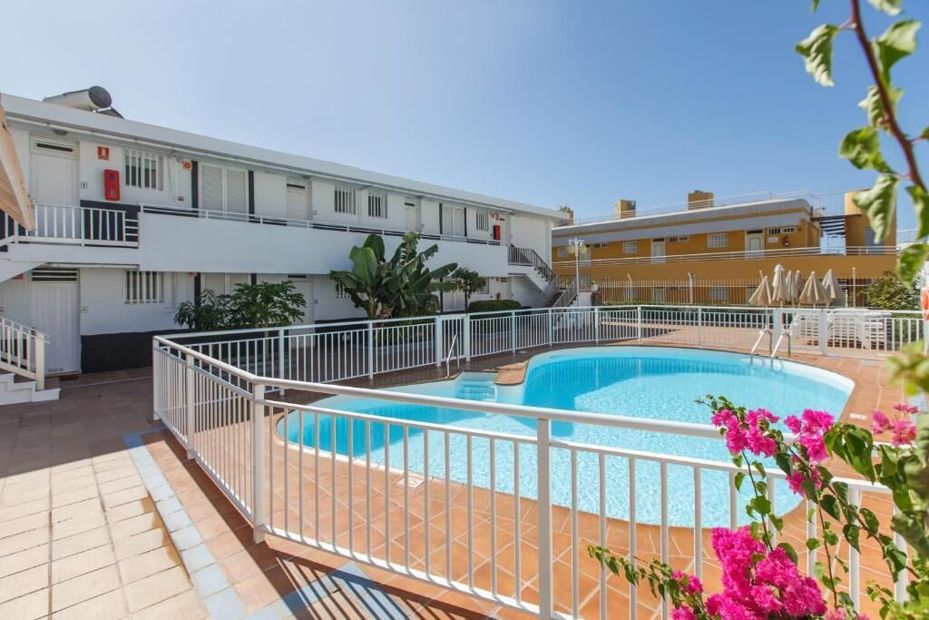 A rooftop swimming pool surrounded by white railings, with a building in the background.