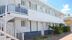 A multi-story building with white exterior walls, a balcony on the second floor, and a small garden area with plants and flowers. - Alsol Las Perlas (San Bartolomé de Tirajana)