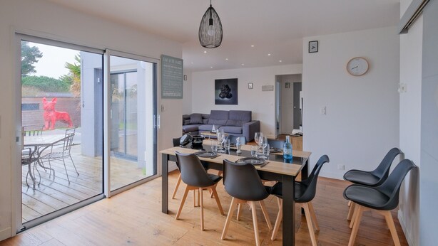 Een moderne eethoek met een glazen deur naar een terras, een grijze bank en een tafel gedekt voor vier personen.