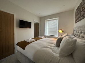 Relax in a spacious bedroom with a large bed, flat-screen TV, and natural light pouring in through the window.