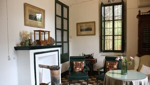 Una habitación con suelo a cuadros, sillones verdes, una mesa redonda con un florero y una chimenea con repisa verde.