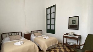Una habitación con dos camas, una silla, una mesa con jarrón y una ventana.