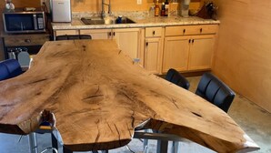 A kitchen with a large wooden table, four chairs, a microwave, a toaster, and wooden cabinets. - Sprague Ranch Cabin: Hill Country Views, Mesquite Firepit, Trails & Pond (Lometa)