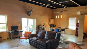 A modern living space with a leather sofa, a dining table, and a kitchen area. - Sprague Ranch Cabin: Hill Country Views, Mesquite Firepit, Trails & Pond (Lometa)