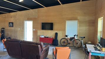 Une pièce spacieuse avec un canapé en cuir marron, un fauteuil orange, un meuble rouge, un vélo et un téléviseur fixé au mur.