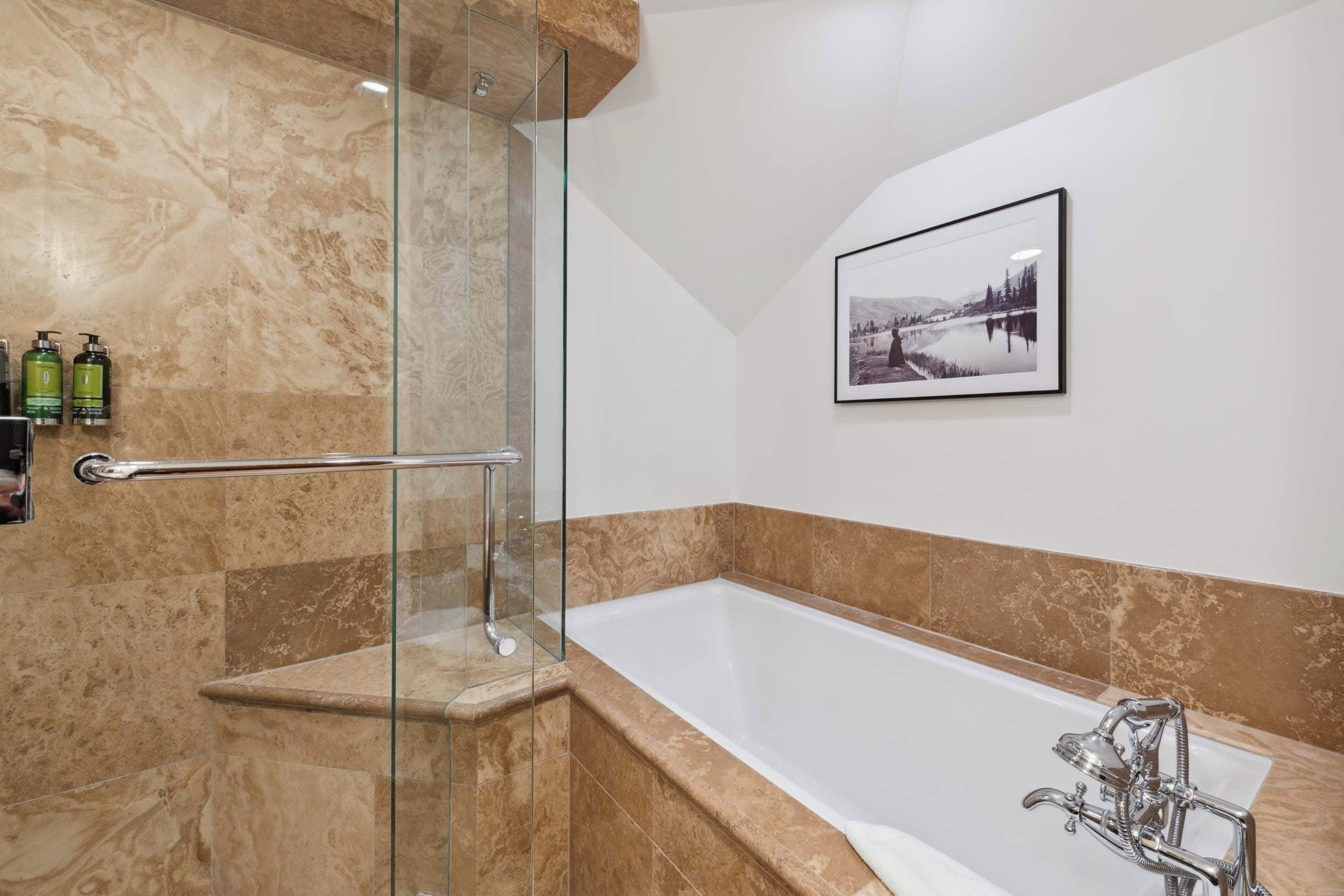 A modern bathroom with a glass shower enclosure, a bathtub, and a framed picture on the wall.