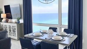 Un coin repas avec vue sur la mer, un lustre et un téléviseur posé sur un meuble blanc.