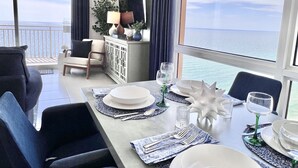 Un coin repas avec vue sur la mer, un canapé, un buffet et une table mise avec des assiettes, des verres et des couverts.