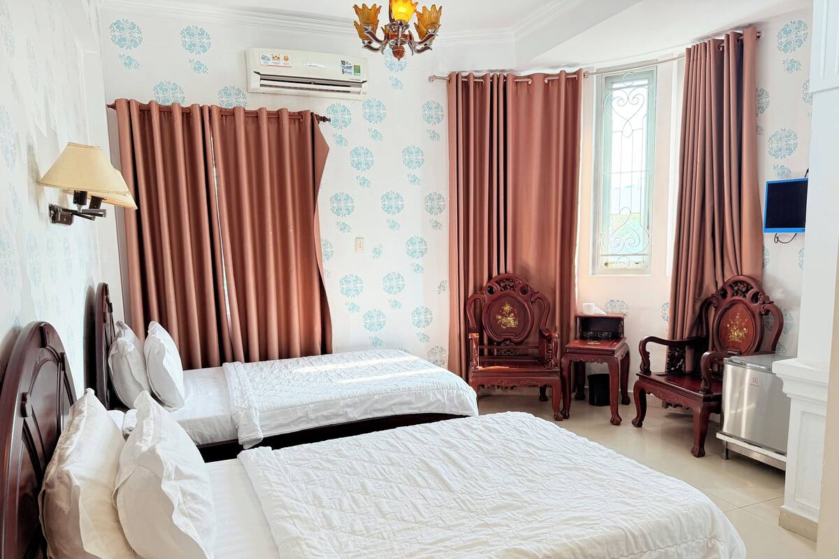 Een hotelkamer met twee bedden, een bureau, een stoel, een airconditioner en een televisie.