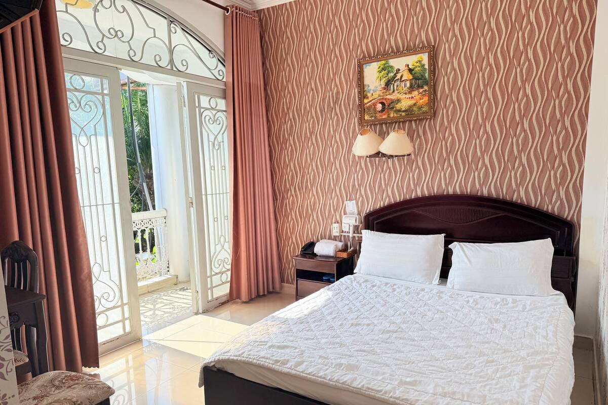 Een hotelkamer met een bed, een nachtkastje, een stoel, een schilderij en uitzicht door een glazen deur.