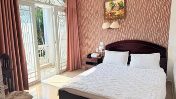 A hotel room with a bed, a nightstand, a chair, a painting, and a view through a glass door.