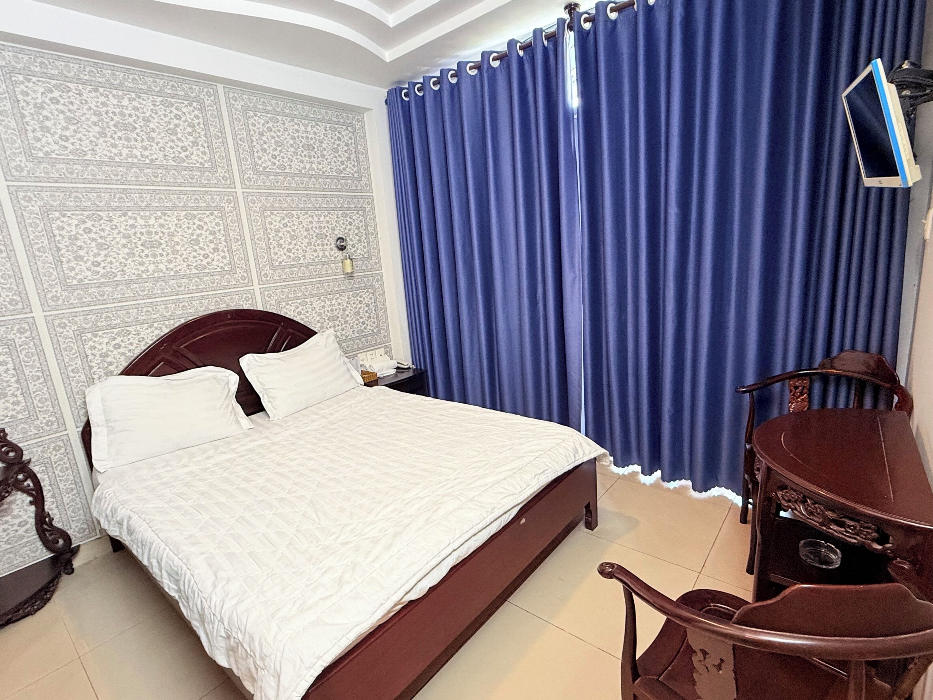 A bedroom with a bed, a nightstand, a chair, and a blue curtain.