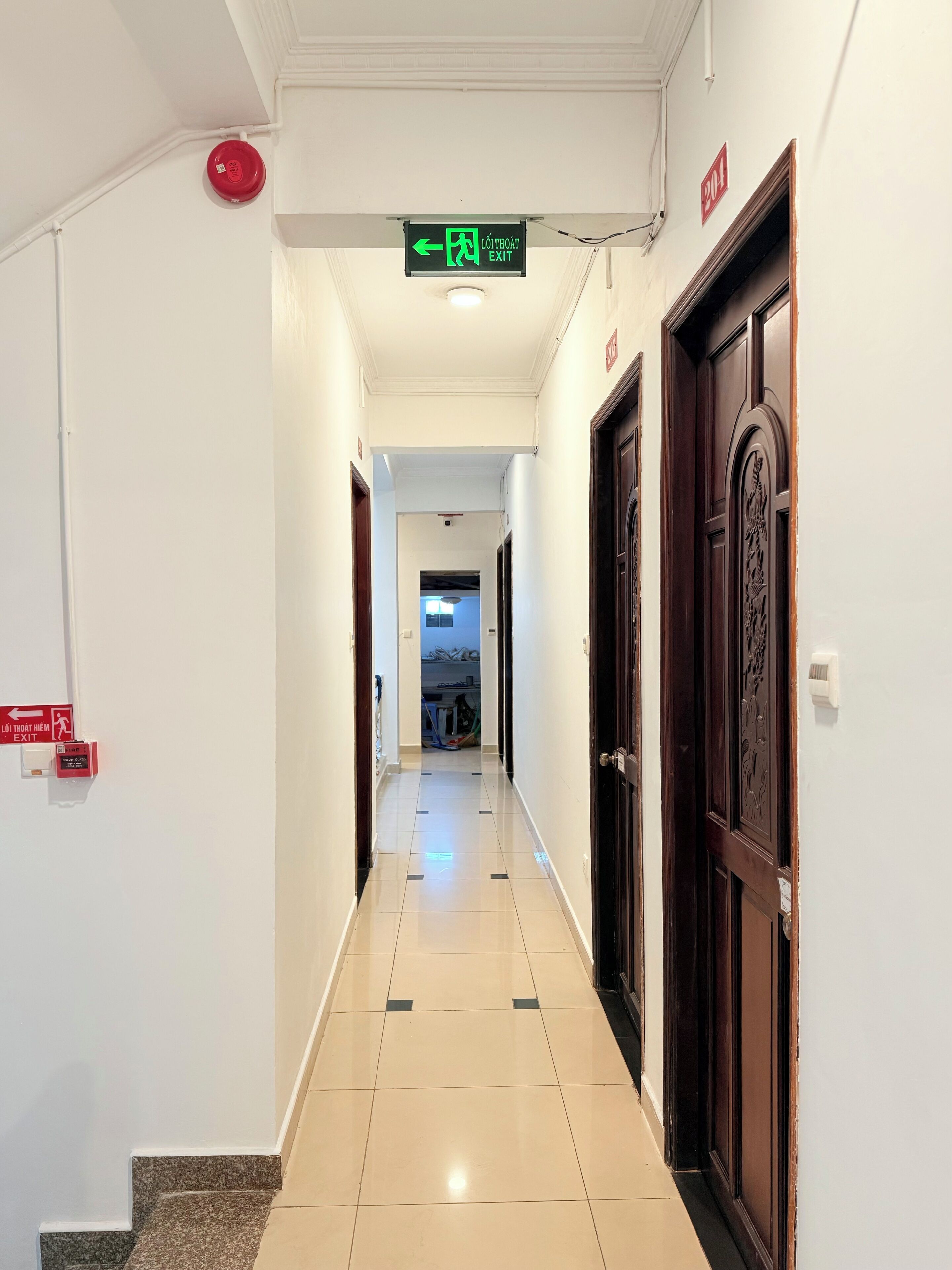 Un couloir d’hôtel avec un panneau de signalisation indiquant clairement la sortie, une alarme incendie et une porte ornée de sculptures complexes.
