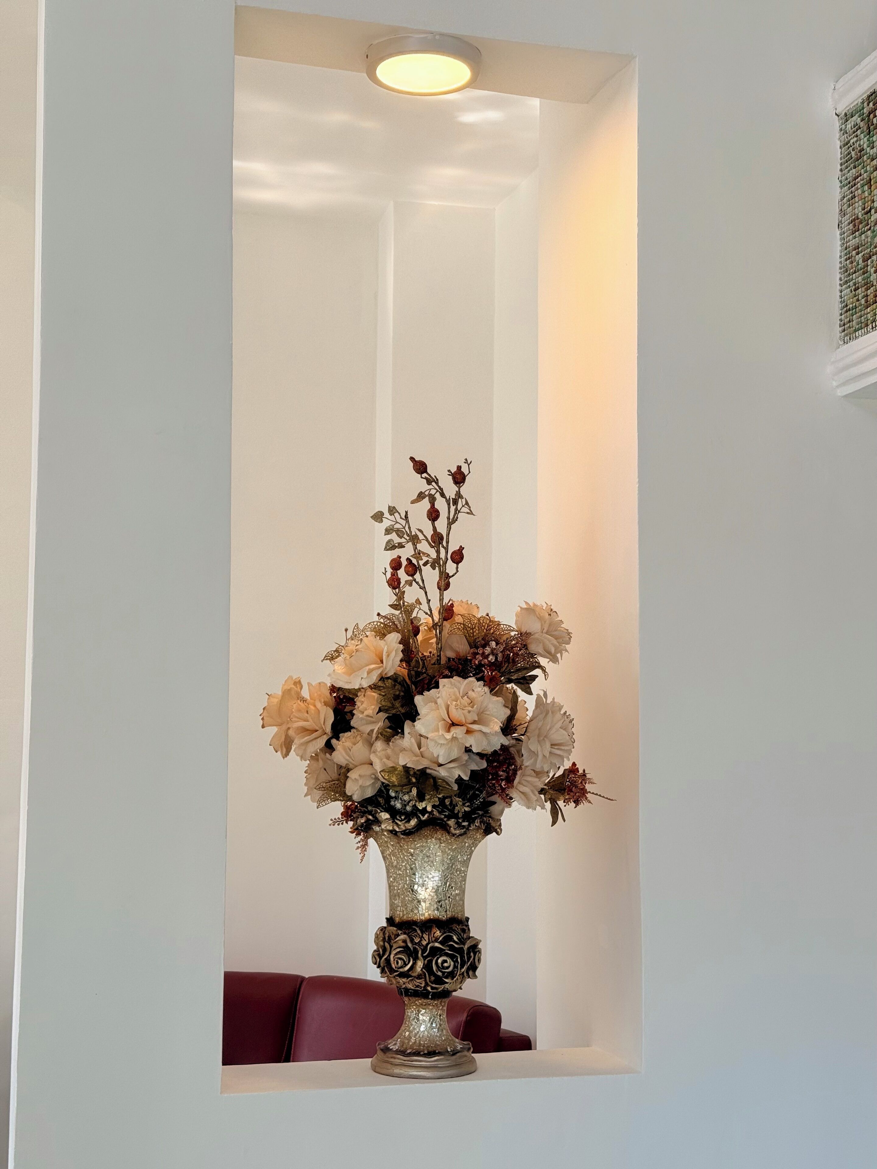 A decorative vase with flowers on a white pedestal in a room with a red couch.