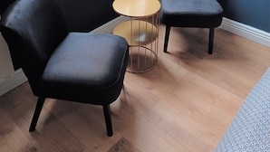 Una habitación con dos sillas tapizadas de color negro, una mesita redonda y un ventanal con vistas a árboles y edificios.