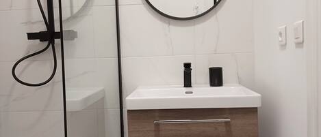 A modern bathroom with a white marble shower, a wooden vanity with a mirror, and a glass-enclosed shower area.