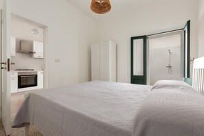 Relax in a spacious bedroom with a large bed, wardrobe, and shower area, plus a fully equipped kitchen nearby.