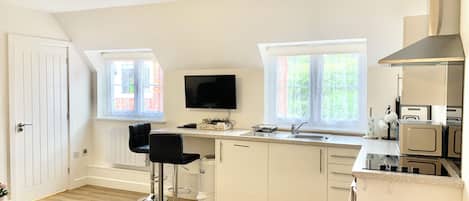 A modern kitchen with a TV, two bar stools, a sink, and a stove.