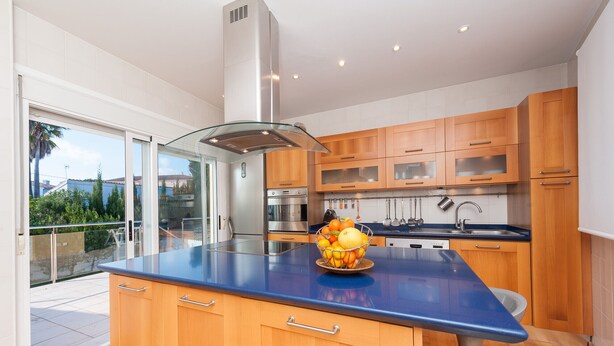 A modern kitchen with wooden cabinets, a blue countertop, and a stainless steel range hood. - Sunset Villa Romani (Ca´n Picafort)