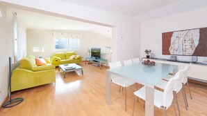 A modern living room with a yellow sofa, a dining table with white chairs, and a large abstract painting on the wall. - Sunset Villa Romani (Ca´n Picafort)