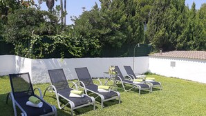 A row of outdoor lounge chairs with towels, set against a white wall and surrounded by greenery. - Sunset Villa Romani (Ca´n Picafort)