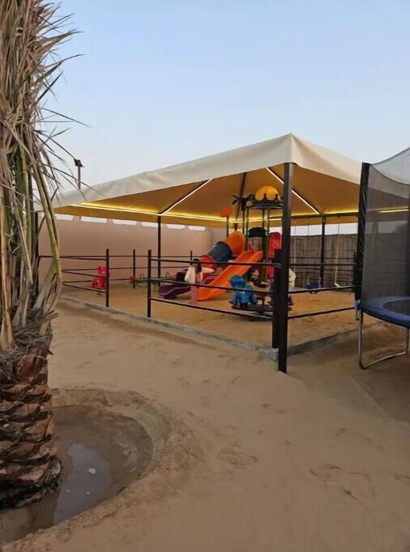 Kids can play under the shaded canopy, featuring a colorful slide and play structure.