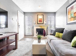 A living room with a sofa, coffee table, fireplace, and a television. - AFFORDABLE APARTMENT WITH BALCONY! (Dallas)