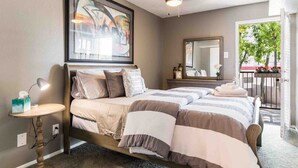 A bedroom with a bed, bedside table, lamp, and a large abstract painting on the wall. - Cute One Bedroom Apartment w. Balcony! (Dallas)