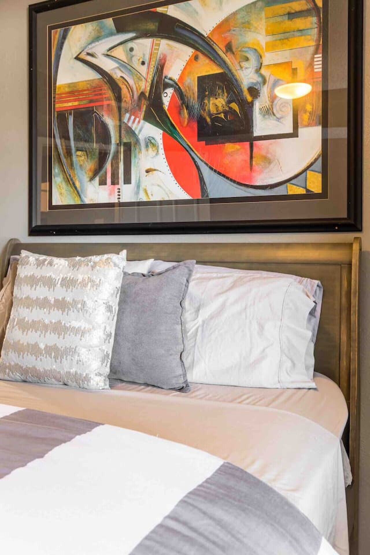 A hotel room with a bed, pillows, and a framed abstract painting above the bed.