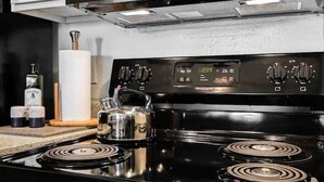 A kitchen with a black microwave, a stove with a kettle, and a digital clock displaying 239. - Cute One Bedroom Apartment w. Balcony! (Dallas)