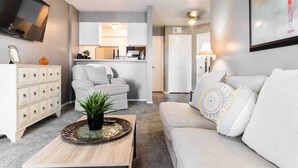 A modern living room with a sofa, a coffee table, and a TV mounted on the wall. - Cute One Bedroom Apartment w. Balcony! (Dallas)