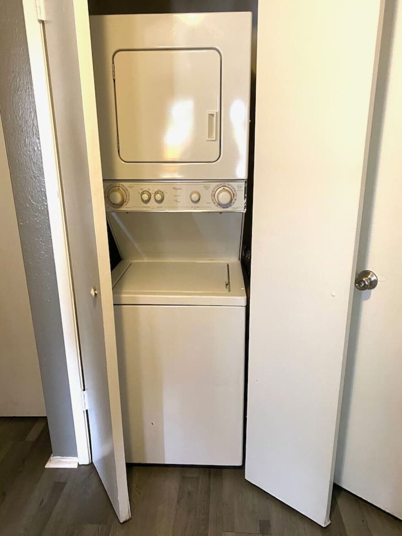 A compact, white laundry room with a built-in washer and dryer, located in a narrow hallway with a door on one side.