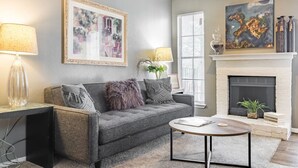 Un salon avec un canapé gris, une table basse ronde, une cheminée et deux tableaux.