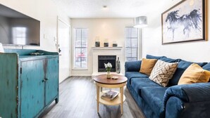 A living room with a blue sofa, a teal cabinet, a fireplace, and a painting. - STAY AWHILE IN THIS COZY 1 BED APT! (Dallas)