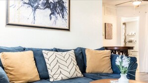 A dark blue sofa with three cushions, a white vase with flowers, and a wooden coffee table. - STAY AWHILE IN THIS COZY 1 BED APT! (Dallas)