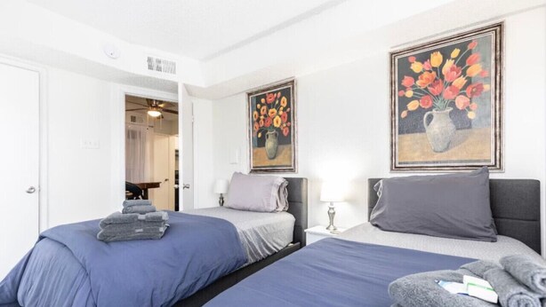 A hotel room with two beds, a nightstand, and two paintings on the wall. - STAY AWHILE IN THIS COZY 1 BED APT! (Dallas)