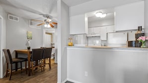A modern kitchen with white cabinetry, a wooden dining table with chairs, and a ceiling fan. - WORK REMOTELY IN URBAN DFW! (Dallas)
