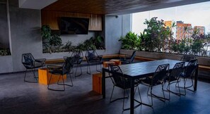 Uma sala de reuniões moderna com uma mesa comprida e cadeiras, rodeada por plantas e vista para a cidade.