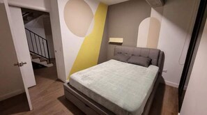 Quarto com cama, luminária na parede e escada que leva a outro cômodo.