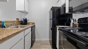 A modern kitchen with white cabinets, a granite countertop, a black refrigerator, and a stove. - Affordable & Convenient! Free WiFi! (Dallas)