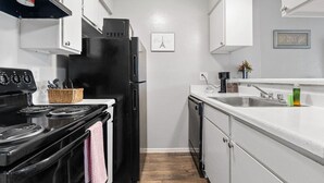 A compact kitchen with white cabinets, a black refrigerator, a stove, and a dishwasher. - One Bedroom Apartment- Access to all DFW! (Dallas)