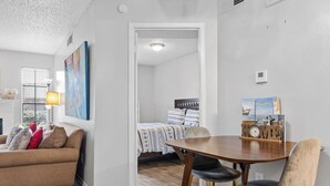 A modern living room with a sofa, a dining table with chairs, and a bed in the background. - One Bedroom Apartment- Access to all DFW! (Dallas)