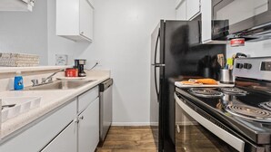 Uma cozinha compacta com armários brancos, geladeira preta, fogão e micro-ondas.